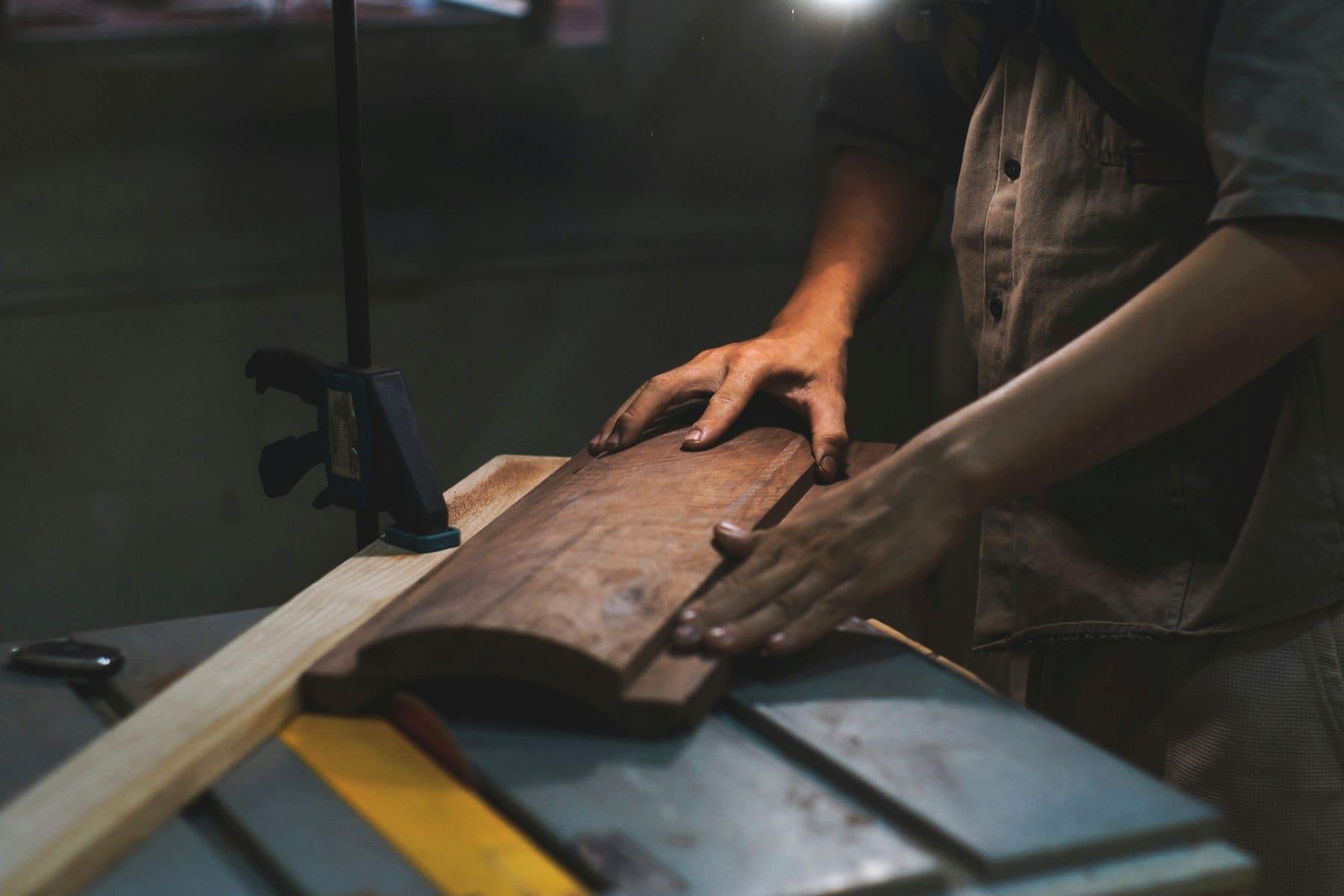 Hände eines Handwerkers führen ein Brett an einer Tischkreissäge in der Werkstatt
